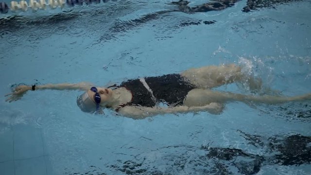 Slow motion of female amateur swimmer practicing backstroke in swimming pool, Full HD sdeadicam shot