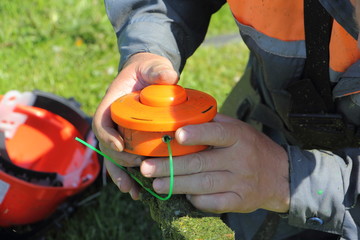 The hands of the lawnmower man holding a spool of garden trimmer - technical service maintenance of...