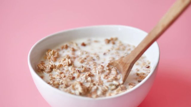 Hand scoop whole grain corn flake from white bowl, pink background and slow motion.
