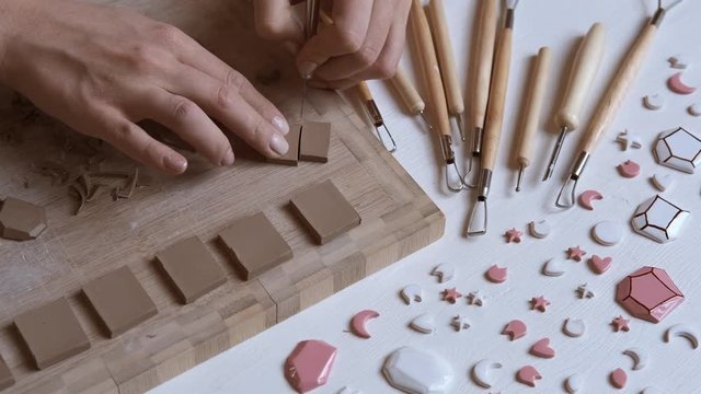 Designer making earrings in workshop. Clay cutting special tool. Female potter master preparing the clay on table. Jewelry designer working in creative studio with tools and materials. Close up 4K
