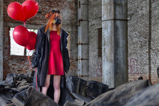 Red hair ginger girl in gas mask, black coat, goggles and red dress, with red helium balloons in hand, staying inside of abandoned brick building with lots of garbage on the floor. Apocalypse scene