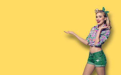 Photo of woman, dressed in pinup style, showing something or copy space, against yellow background