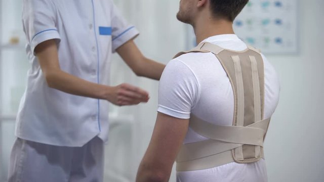 Orthopedist applying posture control shoulder brace male patient, healthcare