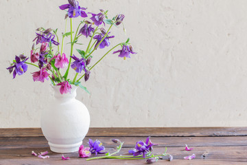 aquilegia flowers in white vase on wooden table