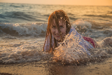 Girl rests and has fun in sea wave at sunset
