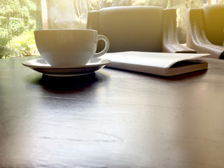 Afternoon tea in white cup with notebook on brown wooden table in the cafe.