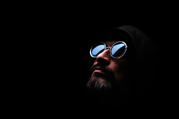 Brutal man in sunglass, with beard, in hood on dark background. Hope.