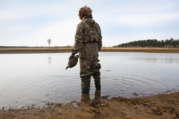 hunter with a duck decoy in his hand stands on the shore