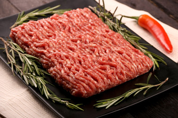 raw minced meat on paper, ingredients for burger with tomato, pepper, onion, spices and seasonings on black background