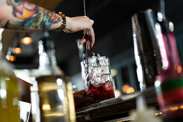 Bartender making refreshing coctail on a bar background. Dark moody style. Ice in tha glass