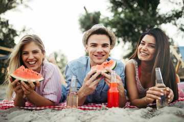 Happy friends having fun on the beach and eating watermelon.