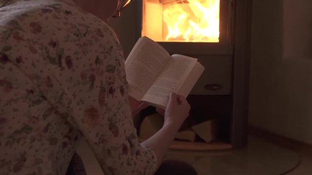 Young woman reading book in living room infront of wood stove