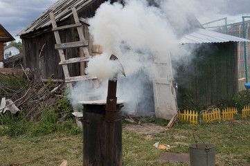 Smoke billows from a stainless steel outdoor furnace.