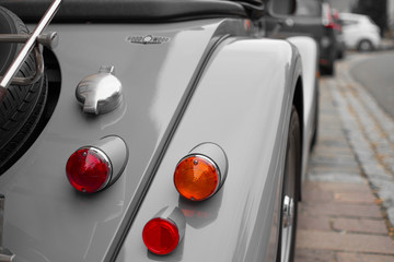 Desatured close up of the rear lights of a classic car parked in the street