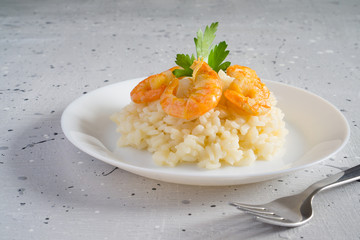 Risotto with shrimps and parsley on a white plate on a light gray background with copy space....