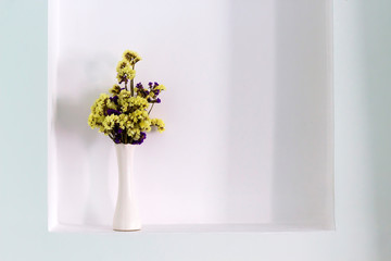 Yellow and violet dried flowers in white vase in light wall niche. Close-up, copy space