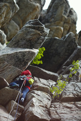 Young woman climber climbs up the rock against the backdrop of rocky overhangs and ledges.  Female rock climber.