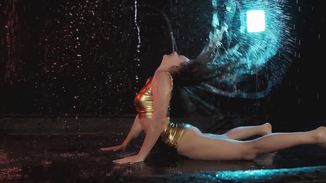 Sexy brunette girl dancing lying on floor. Girl in shorts dance in studio with rain. Girl masterly dancing
