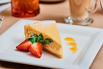 Cheesecake with strawberries on a white plate on the table in a restaurant close up. space