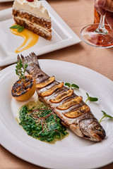 Grilled mackerel with lemon slices and spinach sauce on a white plate on a table in a restaurant. View from above. Close-up