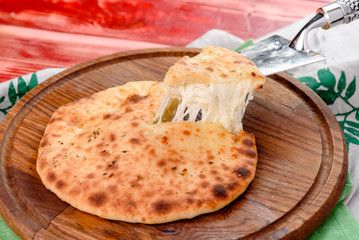 Traditional Georgian dish - Khachapuri with cheese on a round wooden board on a red wooden background, decorated with napkins, chili pepper and cherry tomatoes. close-up