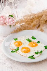 Sunny Side Up Eggs with greens on white plate on wooden table, view from above. Beautiful light composition with fresh roses. Close up. Space