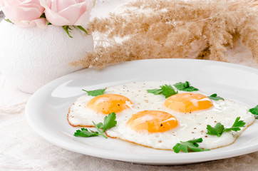 Sunny Side Up Eggs with greens on white plate on wooden table, view from above. Beautiful light composition with fresh roses. Close up. Space