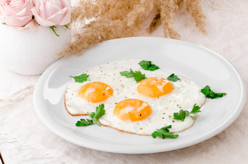 Sunny Side Up Eggs with greens on white plate on wooden table, view from above. Beautiful light composition with fresh roses. Close up. Space