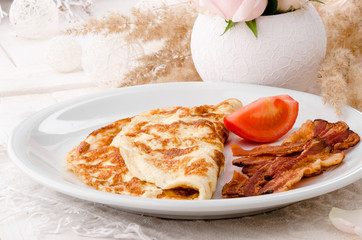 Omelet with crispy fried bacon and tomatoes on white plate on wooden table, view from above. Beautiful light composition with fresh roses. Close up. Space