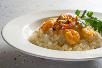Risotto with shrimps and parsley on a white plate on a light gray background with copy space. Italian food