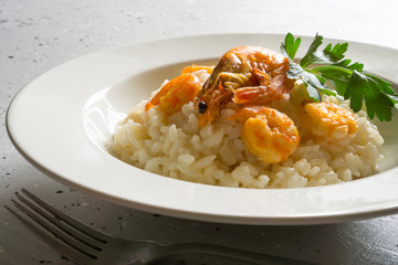 Risotto with shrimps and parsley on a white plate on a light gray background with copy space. Italian food