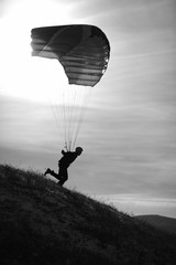 Silhouette of a speedflyer with a parachute running down the hillside, close-up, black and white.