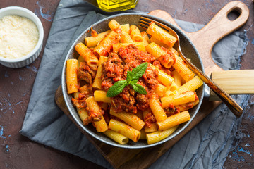 Delicious rigatoni pasta with italian tomato meat ragu sauce served in a pan on dark brown...