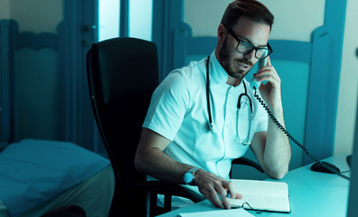 Mid adult doctor making a phone call at doctor's office.