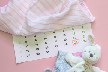 Set of newborn accessories in anticipation of  child - calendar with circled number 27 (twenty seven), baby clothes, toys on pink background. Flat lay, top view.