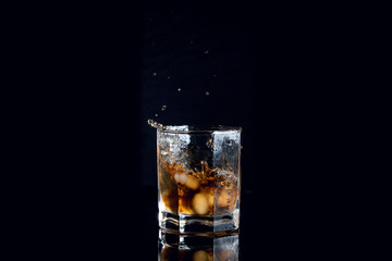 Whiskey splash from the fallen ice cube into glass with beverage isolated on black background..