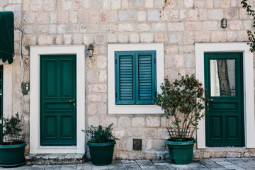 Fototapeta na wymiar Frontal view of a stone residential building with entrance door and windows with shutters and decorated with plants.