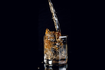 Whiskey pouring into glass with ice isolated on black background..