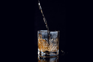 Whiskey pouring into glass with ice isolated on black background..