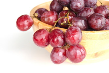 Isolated juicy clusters of large red grapes coiled from a wooden bowl