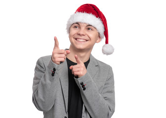 Portrait of smiling teen boy with Christmas hat. Teenager wearing grey suit, pointing and looking upwards. Holiday concept - happy cute child isolated on white background.