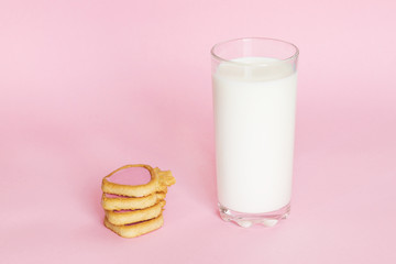 Glass with milk on pink background with cookies