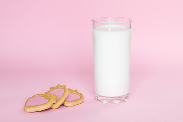 Glass with milk on pink background with cookies