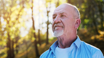 Portrait of senior man with a beard smiling while standing outside in sunlight.