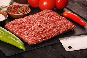 raw minced meat on plate, ingredients for burger with tomato, pepper, onion, spices and seasonings on black background.