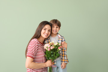 Happy mother and son with bouquet of flowers on color background