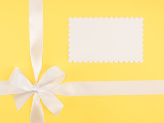 Bow from white satin ribbon on yellow background with copy space