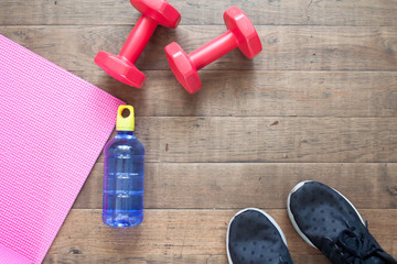 Fototapeta na wymiar Creative flat lay of workout concept. Fitness equipment, water bottle and sport shoes on wooden floor