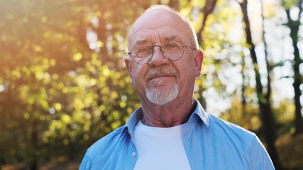 Portrait of senior man with a beard smiling while standing outside in sunlight.