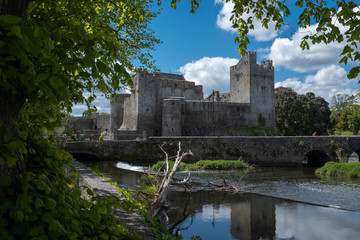A view of the Castle of Cahir across the weir down the River Suir, bright blue sky and fluffy white clouds, nobody in the image